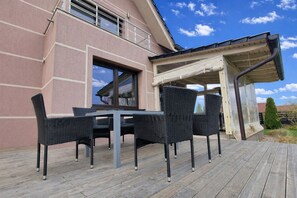 Une terrasse extérieure avec une table et des chaises, un espace abrité et un bâtiment à la façade rose.
