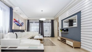 A modern living room with a sofa, a coffee table, a TV, and a large window with curtains. - Spacious 6-bedroom villa in gorgeous Králův Dvůr with fitness room and terrace (Králův Dvůr)