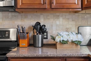 A kitchen with granite countertops, wooden cabinets, a stainless steel microwave, and a flower arrangement.