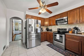 A modern kitchen with stainless steel appliances, wooden cabinets, and a ceiling fan.