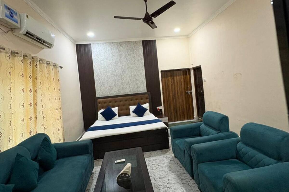 A hotel room with a bed, two sofas, a coffee table, a ceiling fan, and an air conditioning unit.