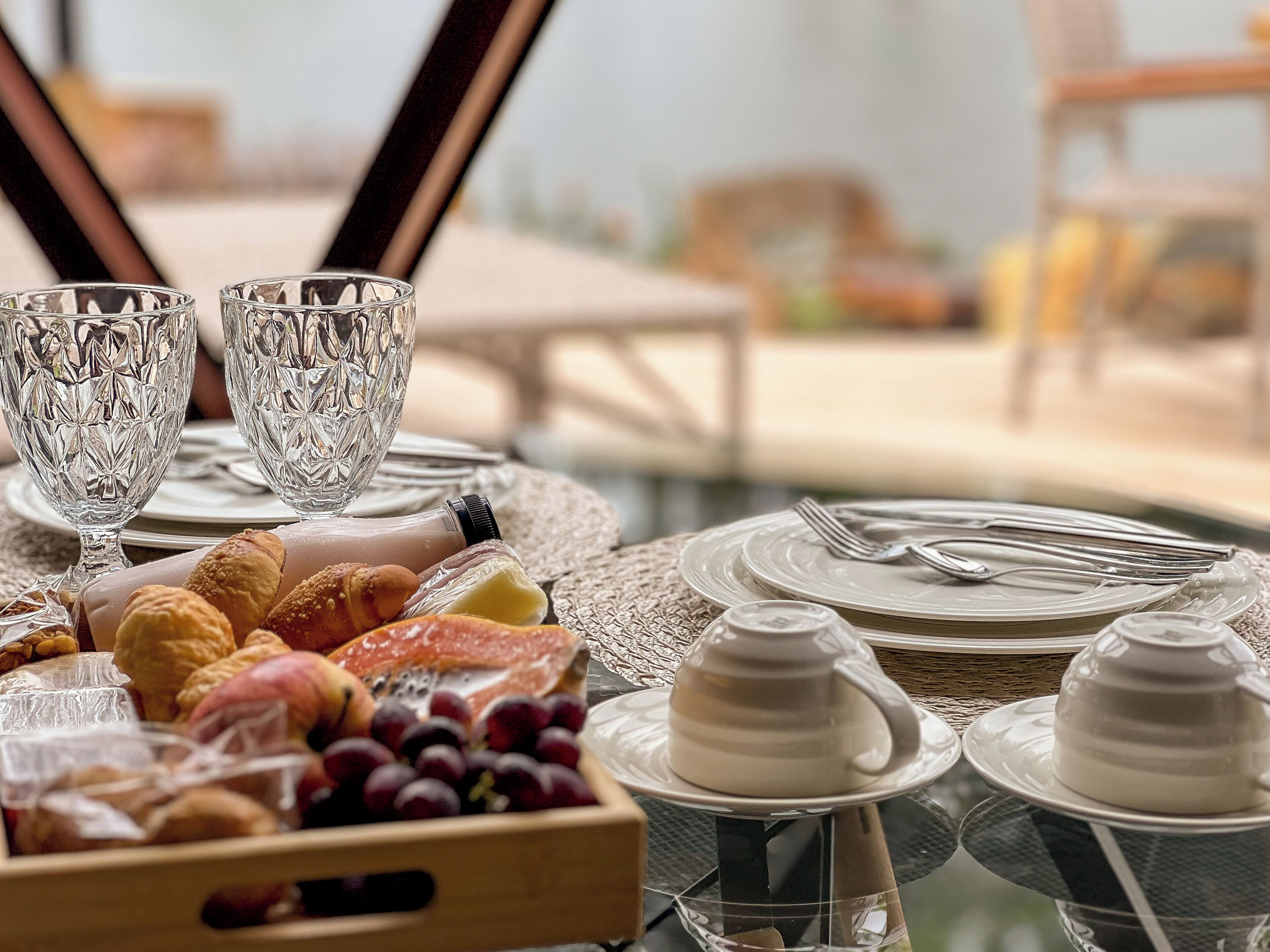 A table set with clear glassware, plates, and a variety of food items including pastries and fruits.