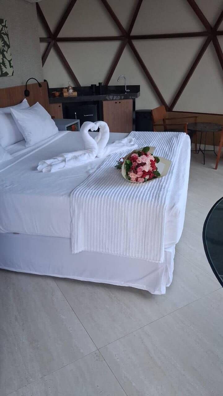 Quarto de hotel com uma cama, um buquê de flores e uma parede com padrão geométrico.