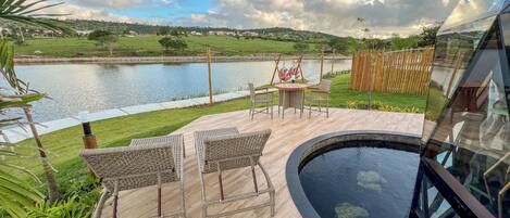 A deck with wicker furniture, a small pool, and a view of a lake and hills.