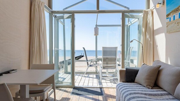 Ein Zimmer mit Glastür und Blick auf einen Strand, ein Bett, ein Tisch und ein Stuhl.