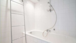 A white tiled shower area with a bathtub and a metal shower ladder. - 3-bedroom apartment in National Residence (Belgium)