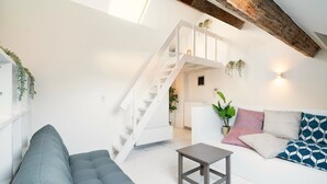 A modern living room with a grey sofa, a small table, a staircase, and a white ceiling. - 3-bedroom apartment in National Residence (Belgium)