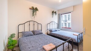 Een kamer met twee bedden, een bloempot en een raam met uitzicht op gebouwen.