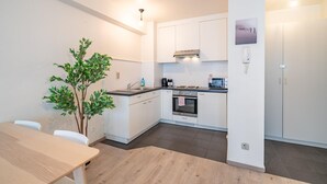 Een moderne keuken met witte kasten, een ingebouwde oven en een eethoek met een houten tafel en stoelen.