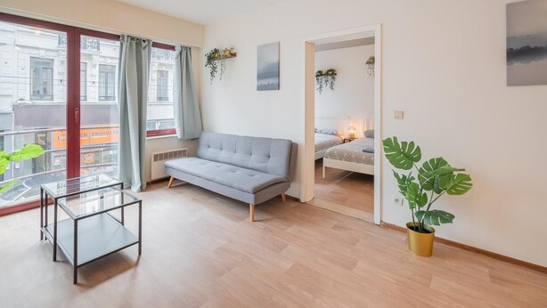 Sala de estar moderna com sofá, mesa de vidro, planta em vaso e vista para o exterior.