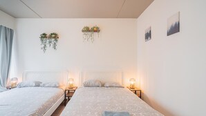 Quarto de hotel com duas camas, abajures, toalha dobrada e vasos de plantas fixados na parede.