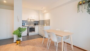 Cozinha moderna com armários brancos, mesa de jantar com cadeiras e um vaso com planta.