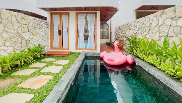 Une maison moderne avec une piscine, des murs en pierre et un flotteur en forme de flamant rose.