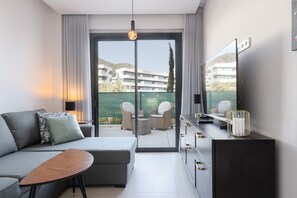 A modern hotel room with a sofa, a small table, a TV, and a balcony with outdoor furniture. - Exclusive Garden Suite in Higueron (Fuengirola)