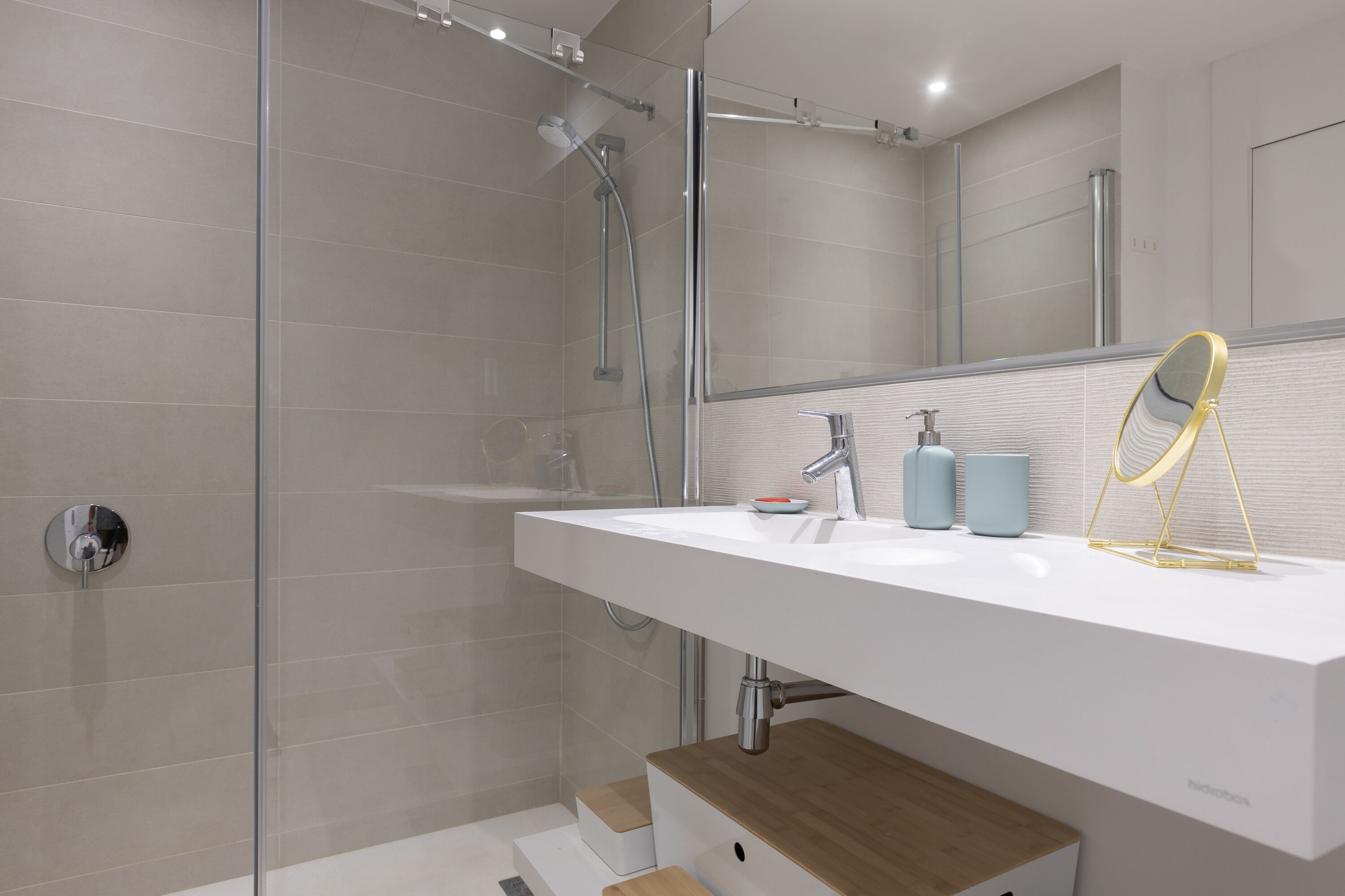 Une salle de bain moderne avec une douche à parois de verre, un lavabo blanc avec un miroir et deux distributeurs de savon bleus.