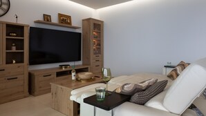 Ett modernt vardagsrum med en platt-TV, träskåp, ett soffbord i glas och en soffa.