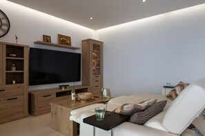 A modern living room with a flat-screen TV, wooden cabinets, a glass coffee table, and a sofa. - Exclusive Garden Suite in Higueron (Fuengirola)