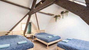 Una habitación con tres camas de madera, una mesita con una lámpara y una ventana con cortinas.