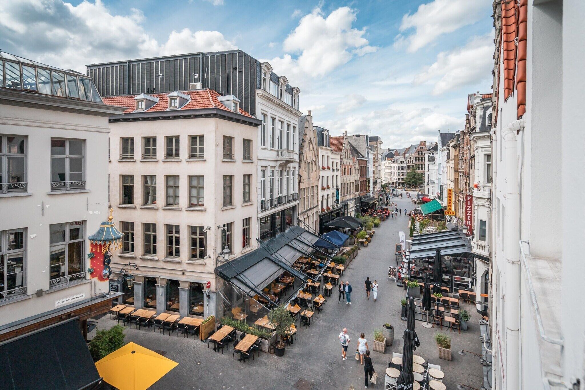 Une rue bordée d’immeubles, avec des terrasses et un ciel dégagé.