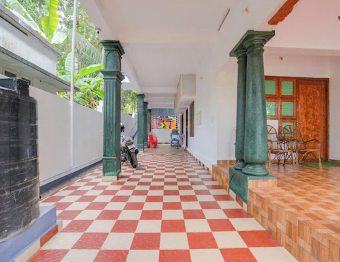 A corridor with checkered flooring, green columns, and a view of a room with a wooden door.