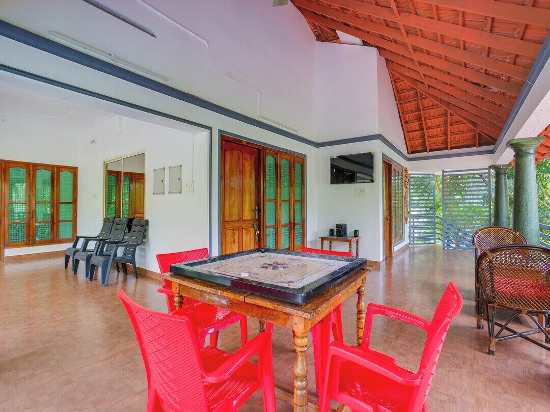 A spacious room with a wooden table and red chairs, large windows with green curtains, and a high ceiling with a wooden beam structure.