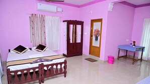 A pink-walled room with a bed, a wooden wardrobe, a table with a checkered tablecloth, and a door with a mirror.