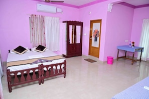 A pink-walled room with a bed, a wooden wardrobe, a table with a checkered tablecloth, and a door with a mirror.