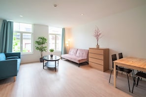 Un salon moderne comprenant un canapé, une table à manger avec des chaises, une petite table ronde avec une plante, et une plante en pot posée sur un meuble.