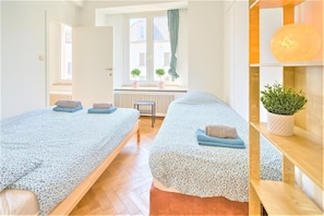 Una habitación con dos camas, una ventana con plantas, un radiador y una estantería con planta.