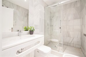 Een moderne badkamer met een douchecabine van glas, een witte wastafel en een toilet.