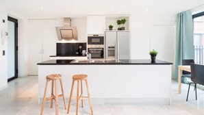 A modern kitchen with a central island, two wooden stools, a refrigerator, and a window with curtains. - 2-bedroom apartment in Central Antwerp (Antwerp Center)