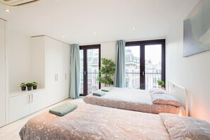 Ein Schlafzimmer mit zwei Betten, einem großen Fenster und Blick auf Gebäude.