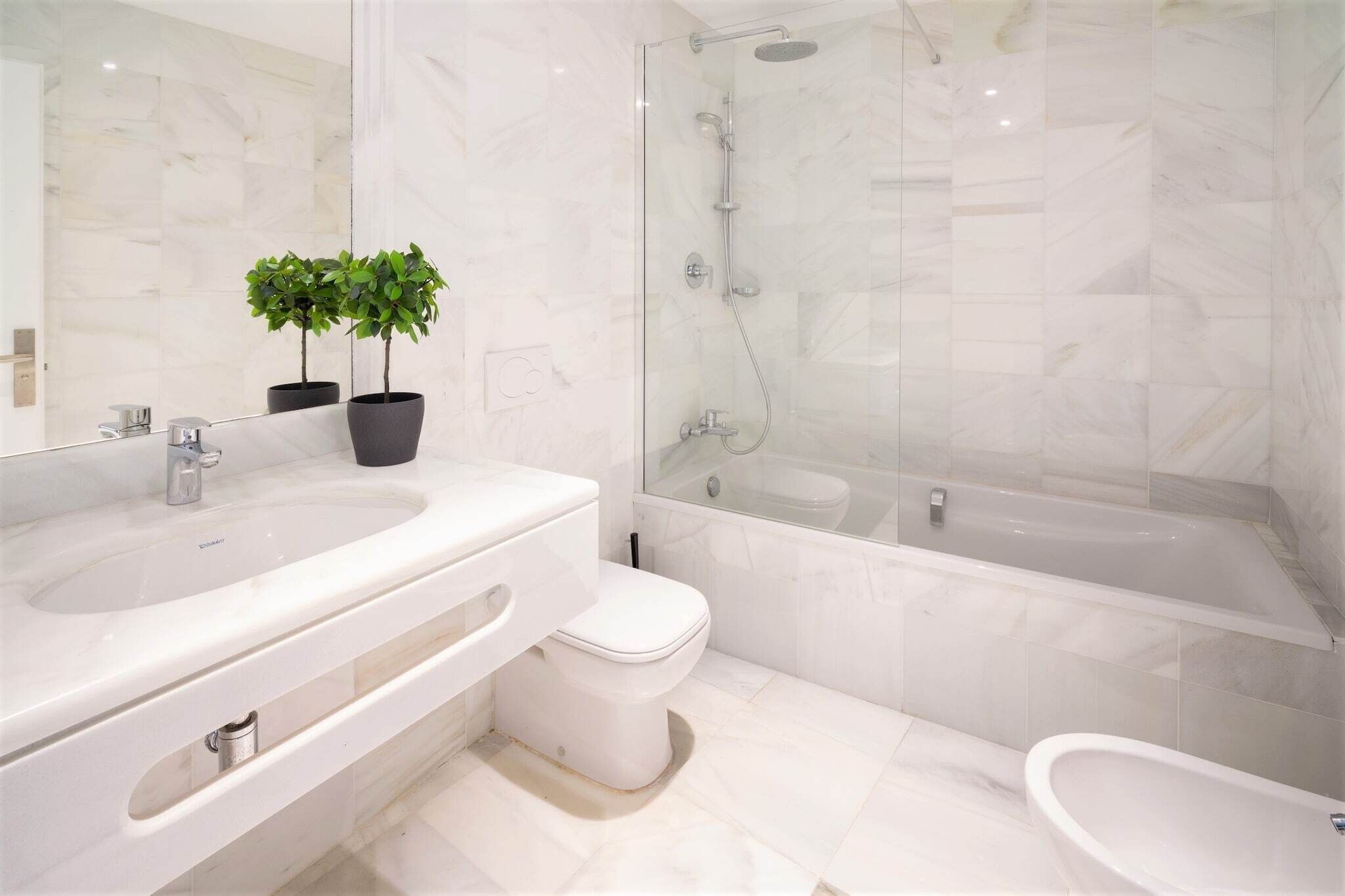 Un baño moderno con ducha envuelta en vidrio, tocador doble y retrete.