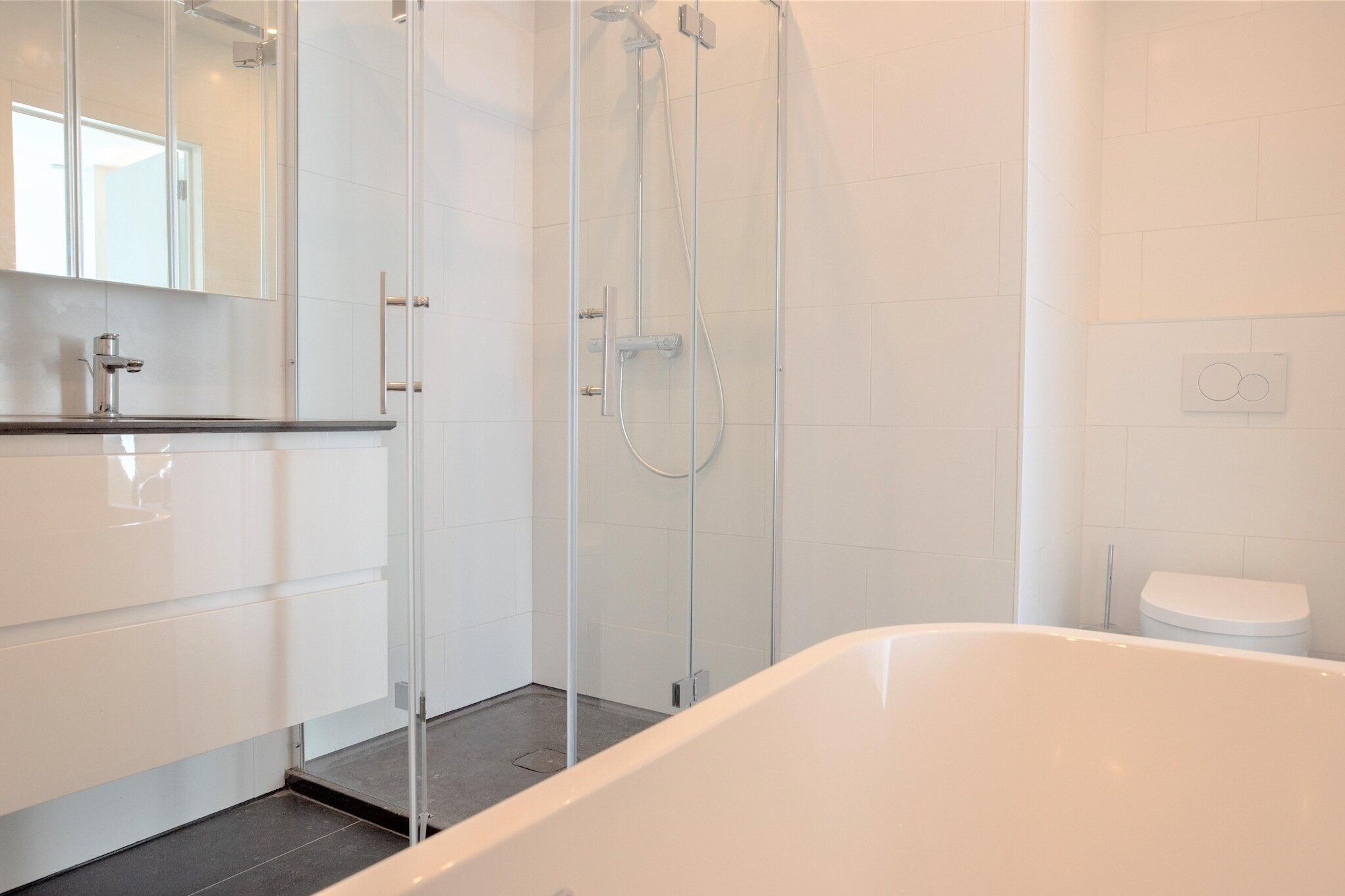 Une salle de bain moderne avec une douche à parois de verre, une baignoire blanche et un grand miroir.
