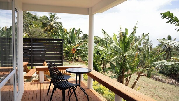 A wooden deck with a table and chairs, surrounded by lush tropical vegetation. - Modern Style Villas 5 Min Walk to the Best beach on the Island
Unlimited WIFI In (Rarotonga)