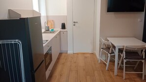 A compact kitchen with a refrigerator, a sink, a white table with chairs, and a door.