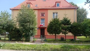 A two-story building with a red-tiled roof, a flag, and a paved entrance.