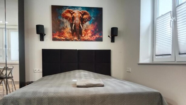 A bedroom with a bed, a painting of an elephant, and two wall-mounted lamps.