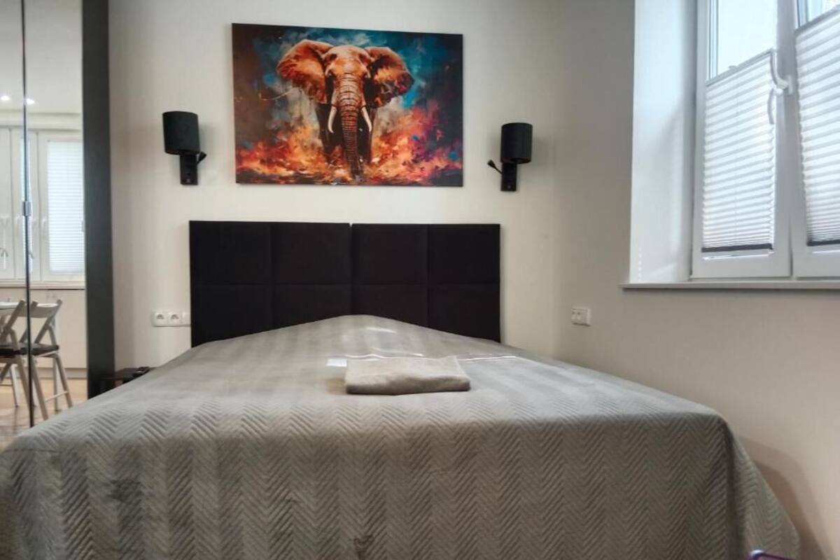 A bedroom with a bed, a painting of an elephant, and two wall-mounted lamps.