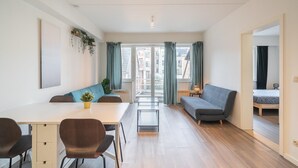 Um apartamento moderno com área de jantar, sofá e vista para prédios através de amplas janelas.