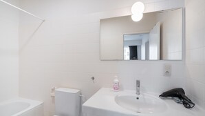Casa de banho com lavatório branco, espelho e sanita.