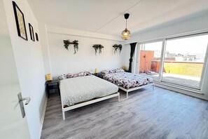 A bedroom with two beds, a sliding glass door to a balcony, and a hanging plant decoration. - Apartment in Antwerp with garden view (Antwerp)