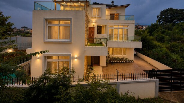 A modern multi-story house with a balcony, a staircase, and a garden area.