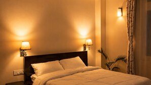 A neatly made bed with a headboard, two bedside lamps, a small table, and a potted plant in a hotel room.
