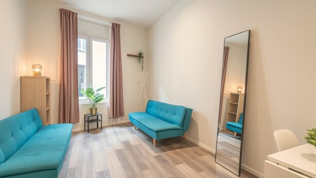 Een kamer met twee banken, een spiegel, een klein tafeltje met een lamp en een plant in een pot.
