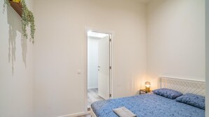 Een slaapkamer met een bed, nachtkastje, lamp en een deur naar een andere kamer.