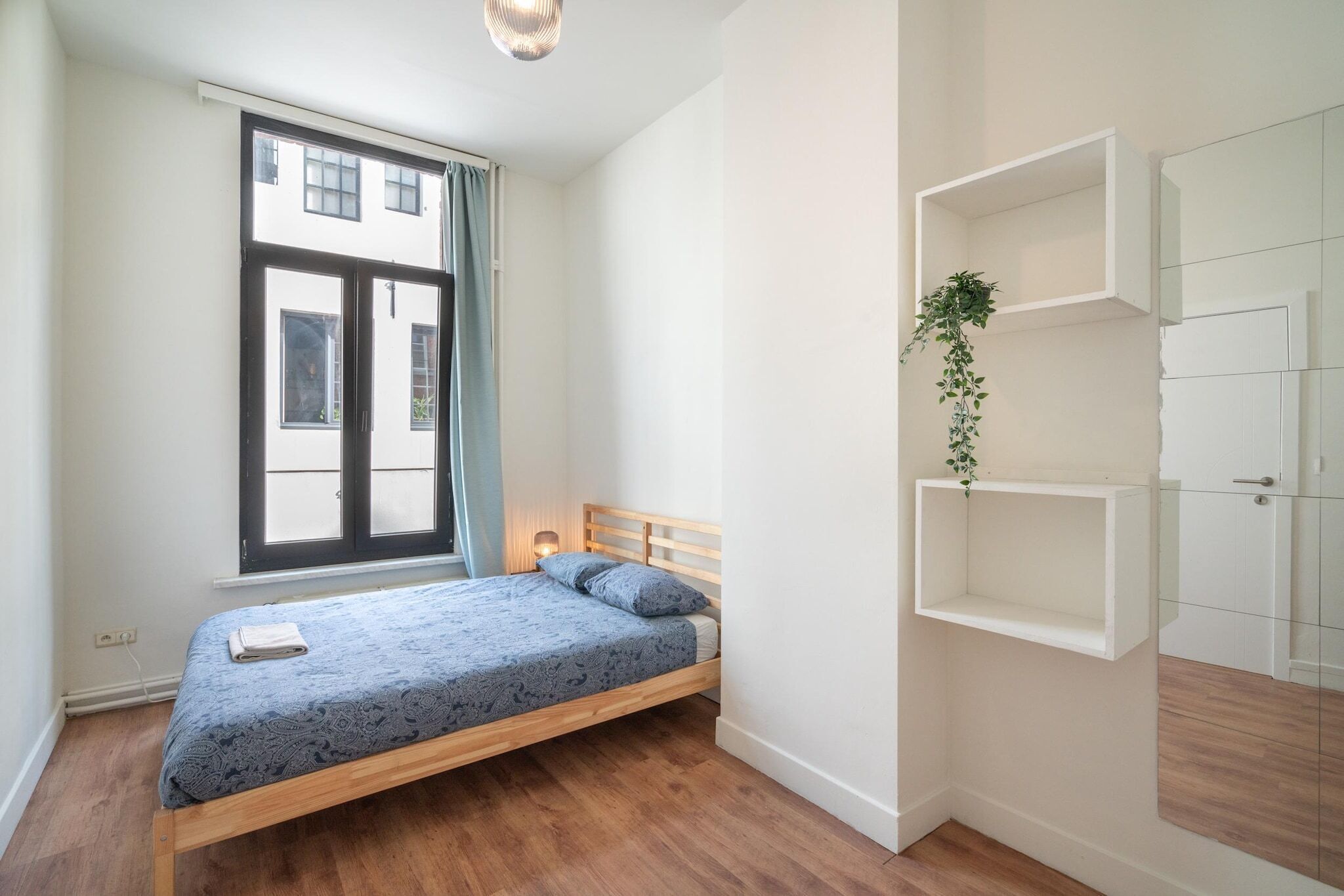Een slaapkamer met een bed, een raam, een wandplank en een deur.