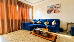 A living room with a blue sofa, a coffee table, a rug, and a painting on the wall. - Le Vintage · Tanger Corniche - Sea view, private parking & terrace (Tangier)