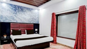 A bedroom with a bed, a nightstand, a window with curtains, and a wall with a textured design. - Hotel Rawat Near Railway Station, Jaipur (Jaipur)
