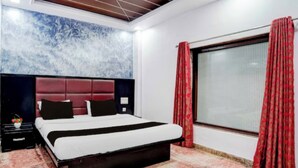 A bedroom with a bed, a nightstand, a window with curtains, and a wall with a textured design. - Hotel Rawat Near Railway Station, Jaipur (Jaipur)